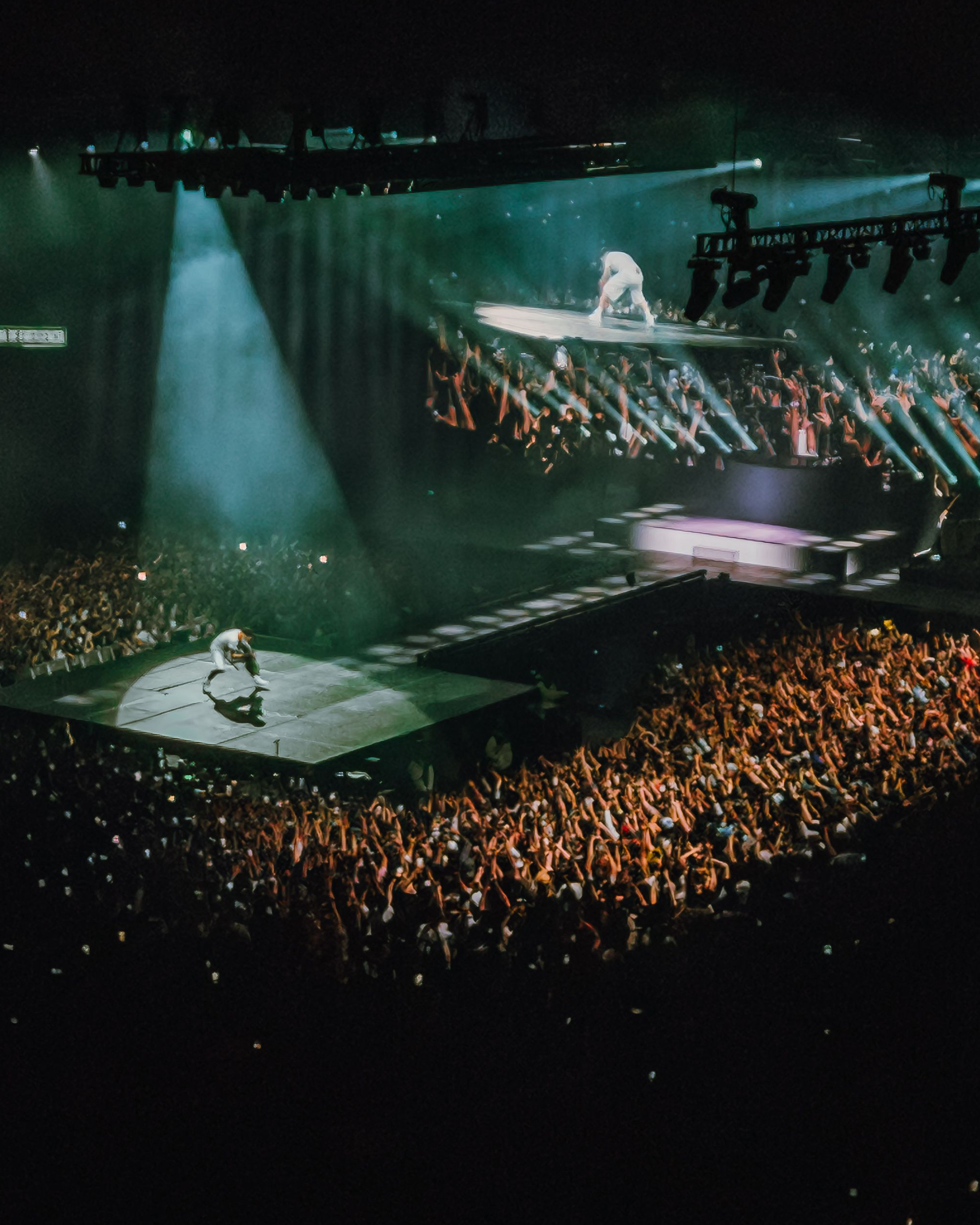An arena from above, two stages lit in teal among the crowd