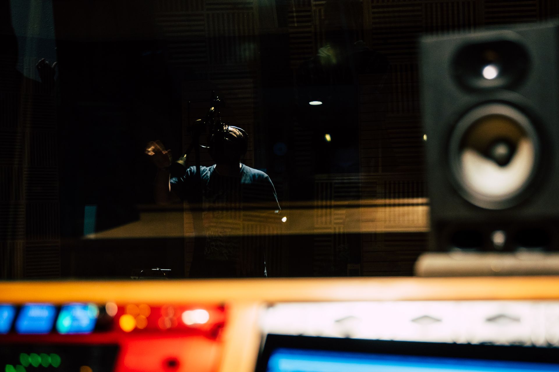 A vocalist seen from the control room, past the monitor and the booth glass