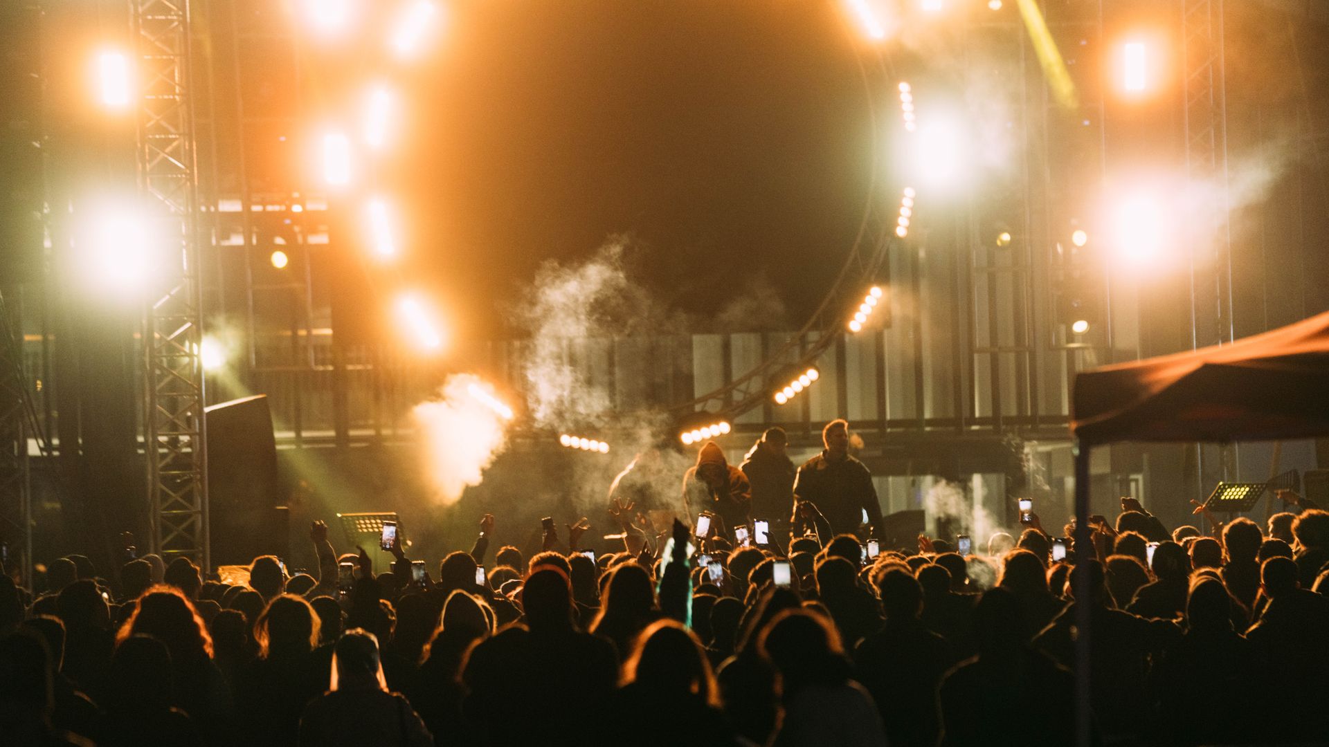 A festival floor in amber, phones up, the stage burning through the smoke